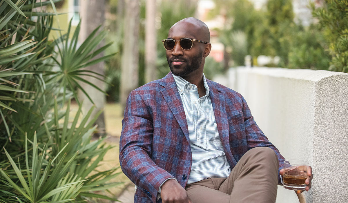 Model wearing a stylish red and blue plaid sport coat holding a drink